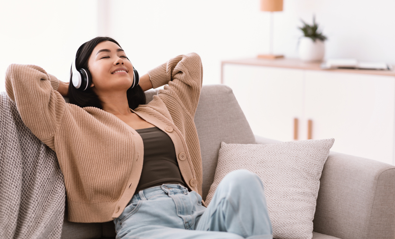 Calm asian lady listening to music wearing headphones